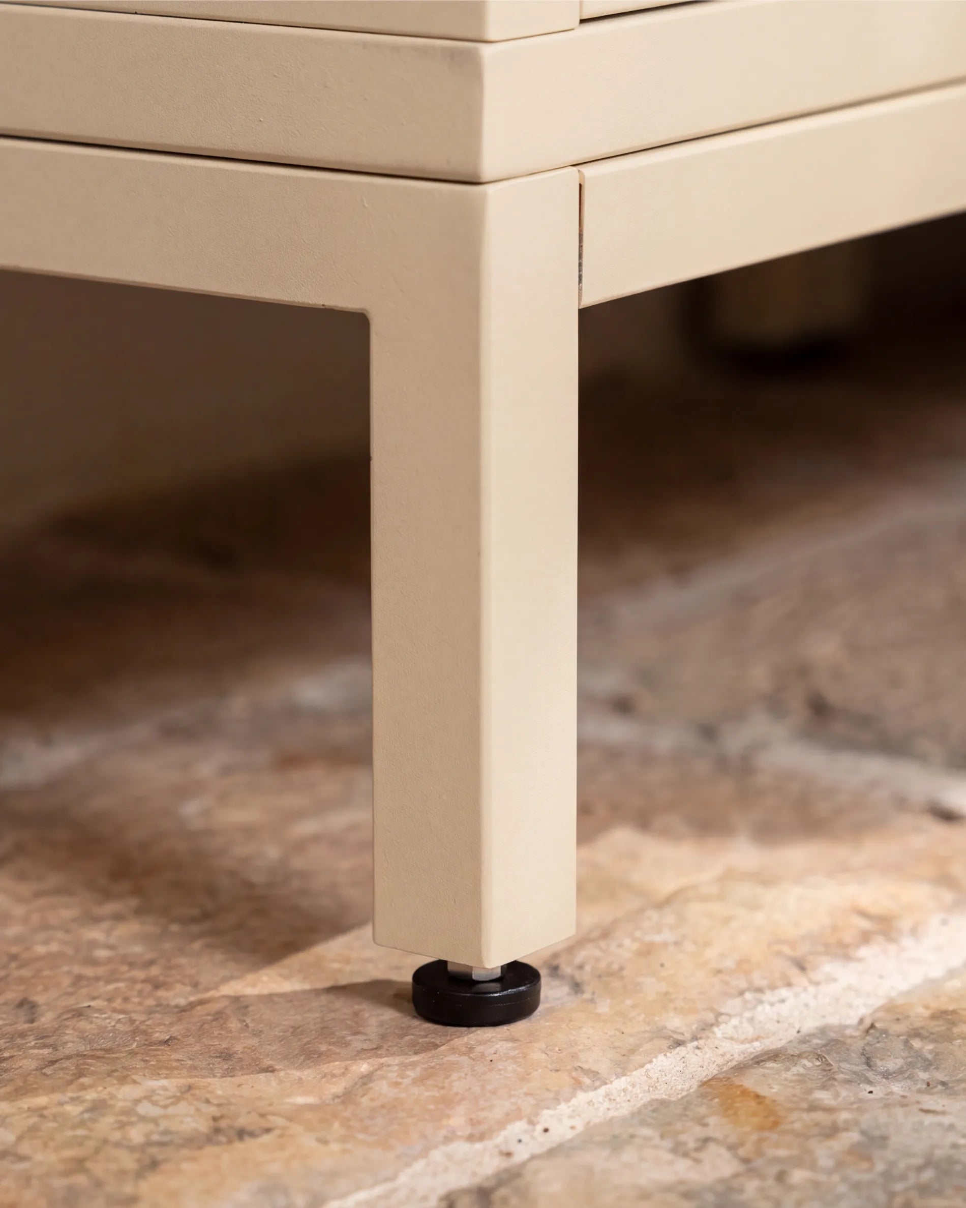 Piede metallico beige crema della struttura PILOTIS con piedino di livellamento, primo piano su pavimento in pietra