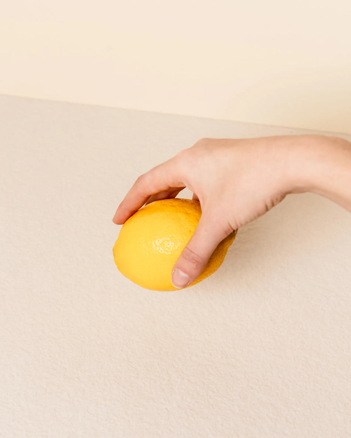 Mano che tiene un limone sopra il piano beige crema del modulo Classic PILOTIS, primo piano