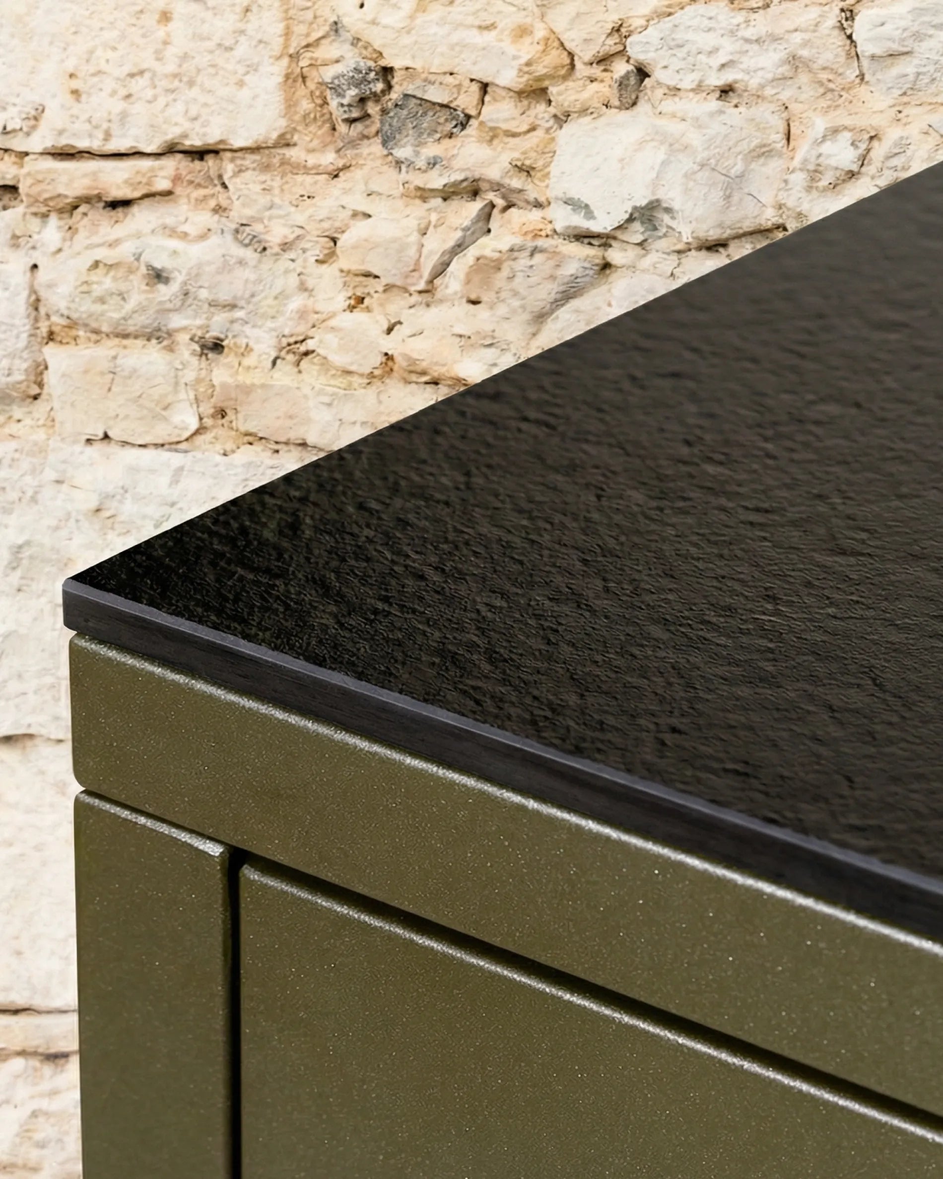 Dettaglio dell’angolo del piano nero PILOTIS, primo piano sul modulo verde oliva accostato al muro in pietra