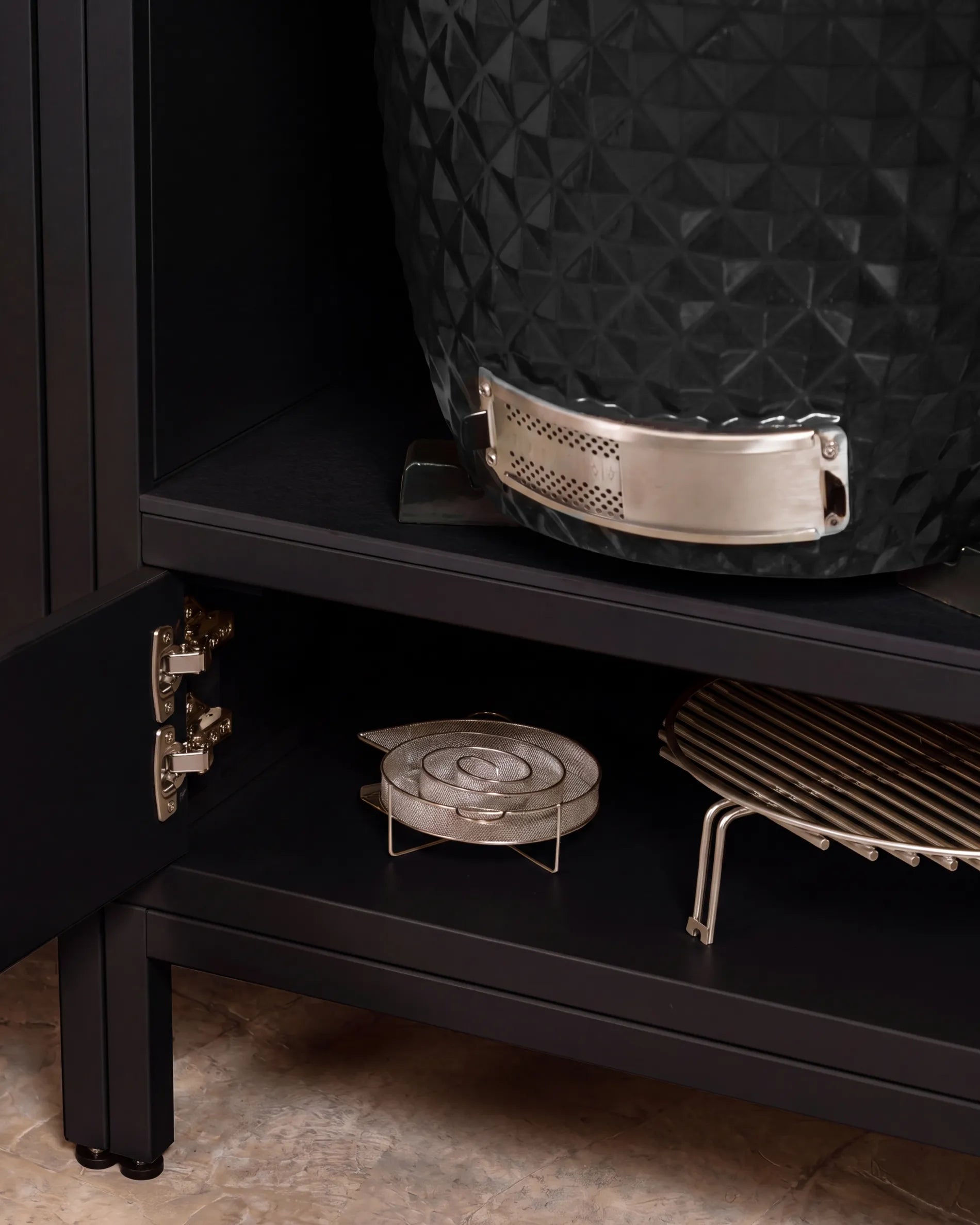 Barbecue kamado nero Kokko inserito nella nicchia del mobile PILOTIS, primo piano sulla cerniera e sulle griglie portaoggetti