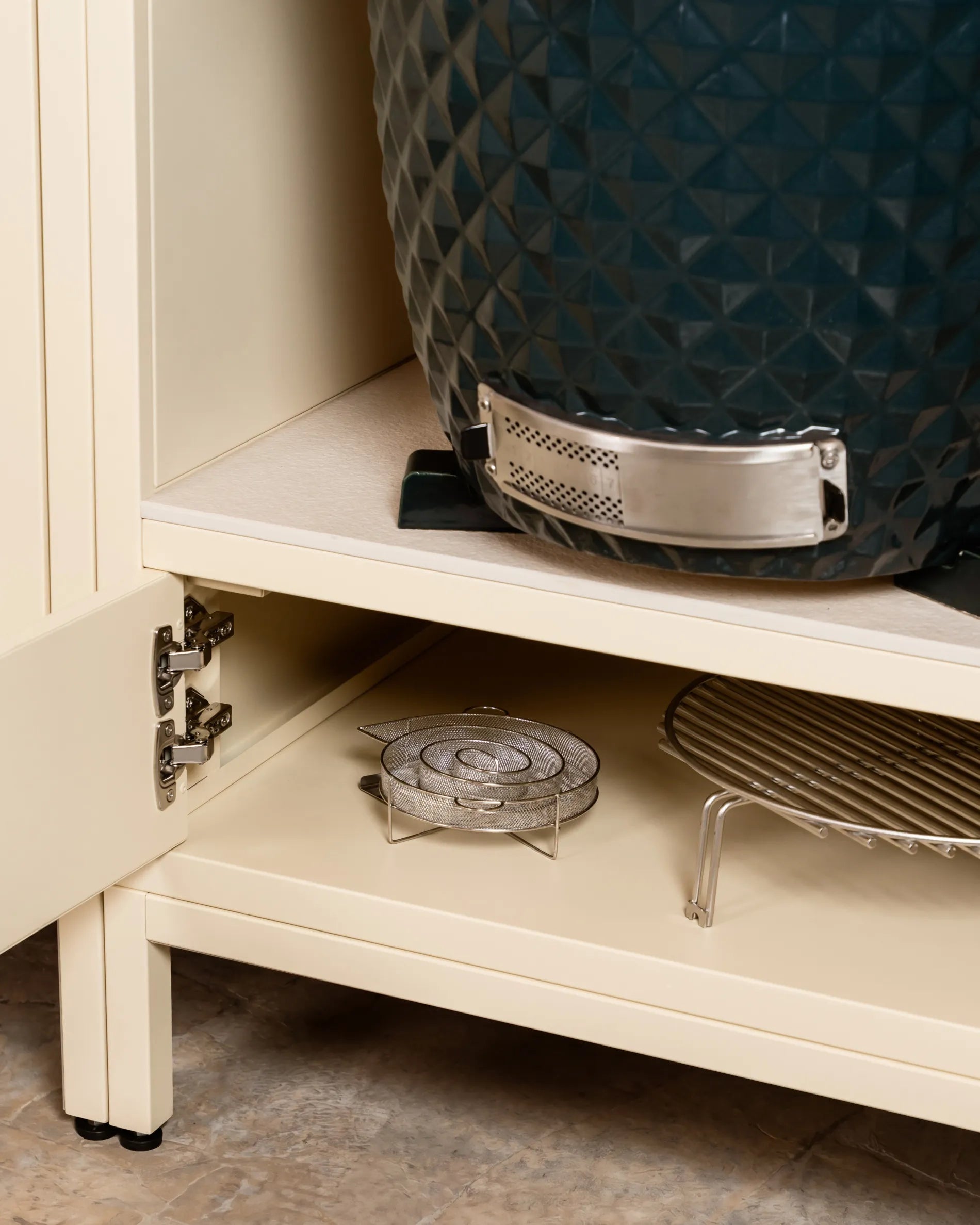 Kamado blu navy Kokko inserito nella nicchia del mobile beige crema PILOTIS, primo piano sulla cerniera e sulle griglie portaoggetti