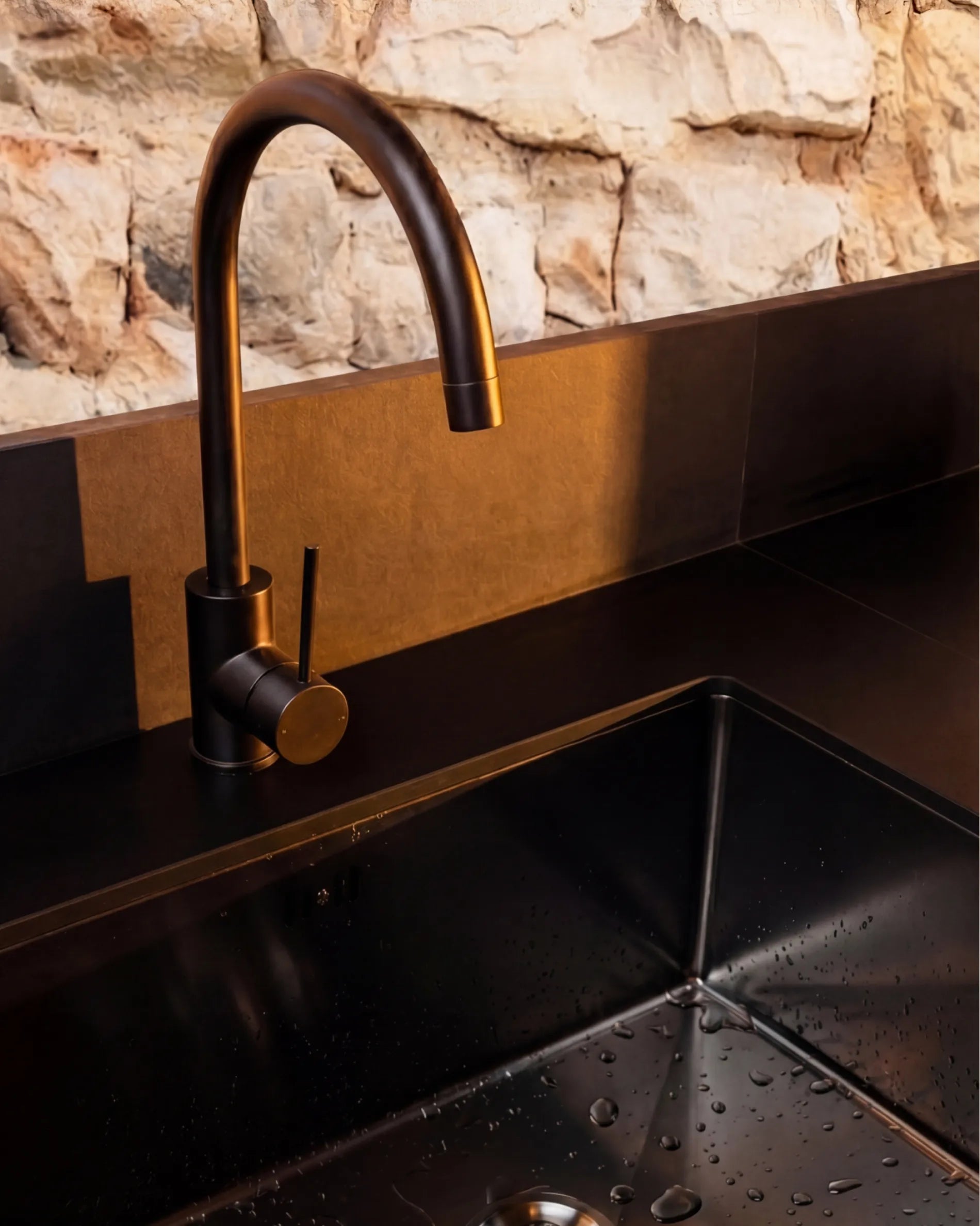 Primo piano sulla vasca nera e il rubinetto con finitura bronzo del modulo Lavello PILOTIS