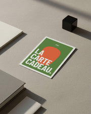 Carta regalo Kokko appoggiata su una superficie minerale, grafica verde e arancione con testo «la carta regalo».
