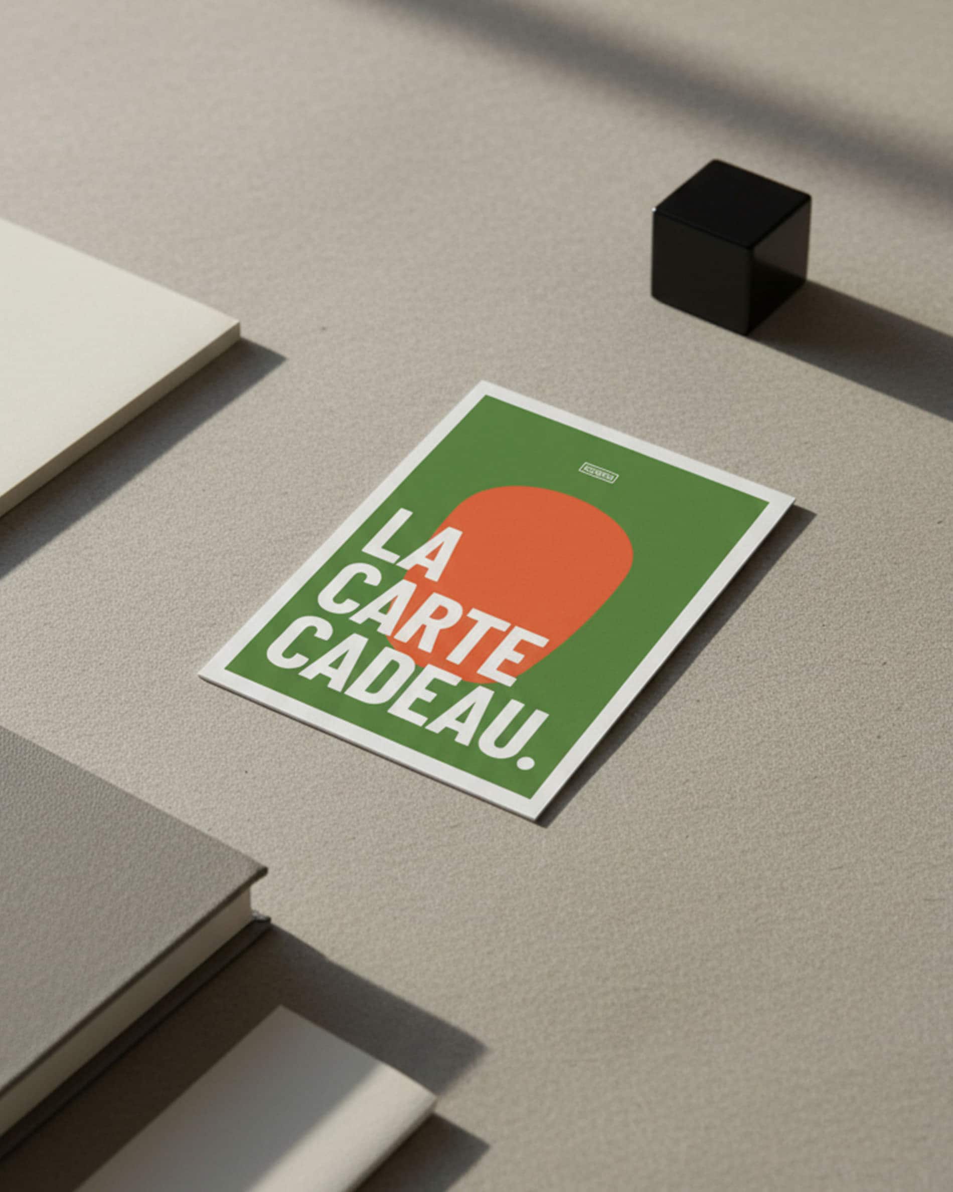 Carta regalo Kokko appoggiata su una superficie minerale, grafica verde e arancione con testo «la carta regalo».