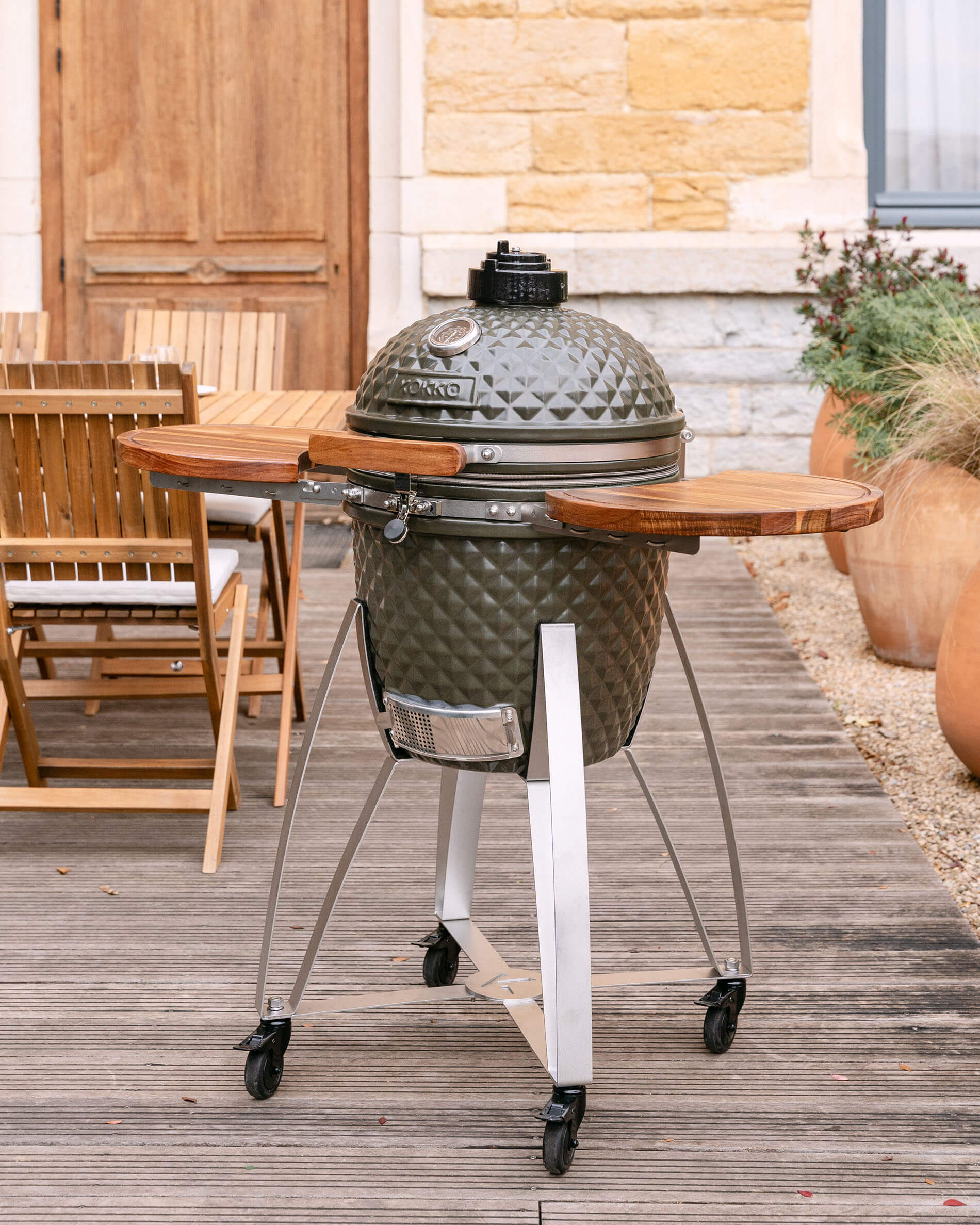 Kamado Kokko su carrello mobile con ripiani laterali in legno, presentato all’aperto su una terrazza.
