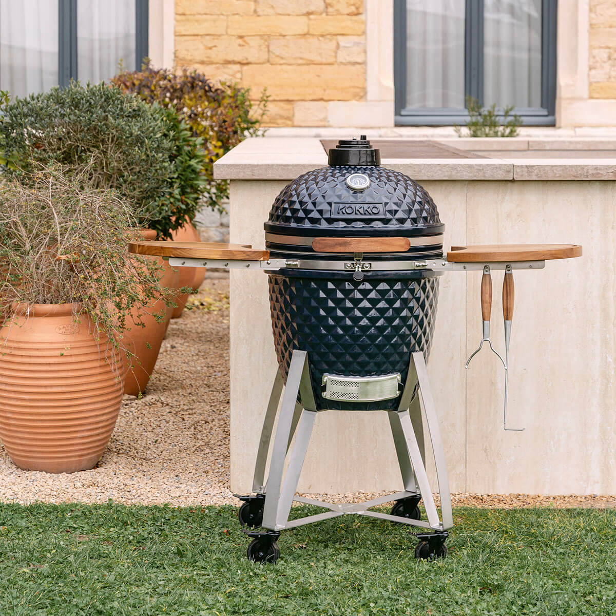 Kamado Kokko navy in ceramica, dotato di ripiani in legno e supporto mobile con ruote.