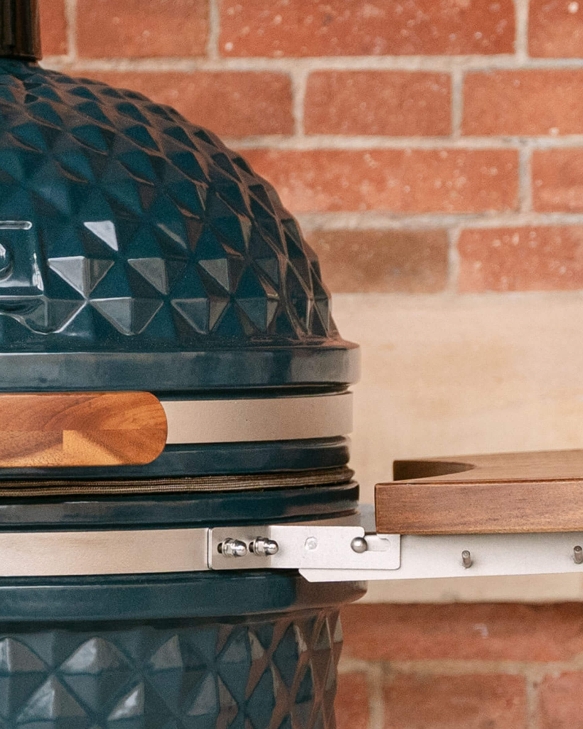 Dettaglio dei fissaggi metallici che collegano un ripiano laterale in legno al corpo del kamado, con viti a vista e guarnizione visibile.
