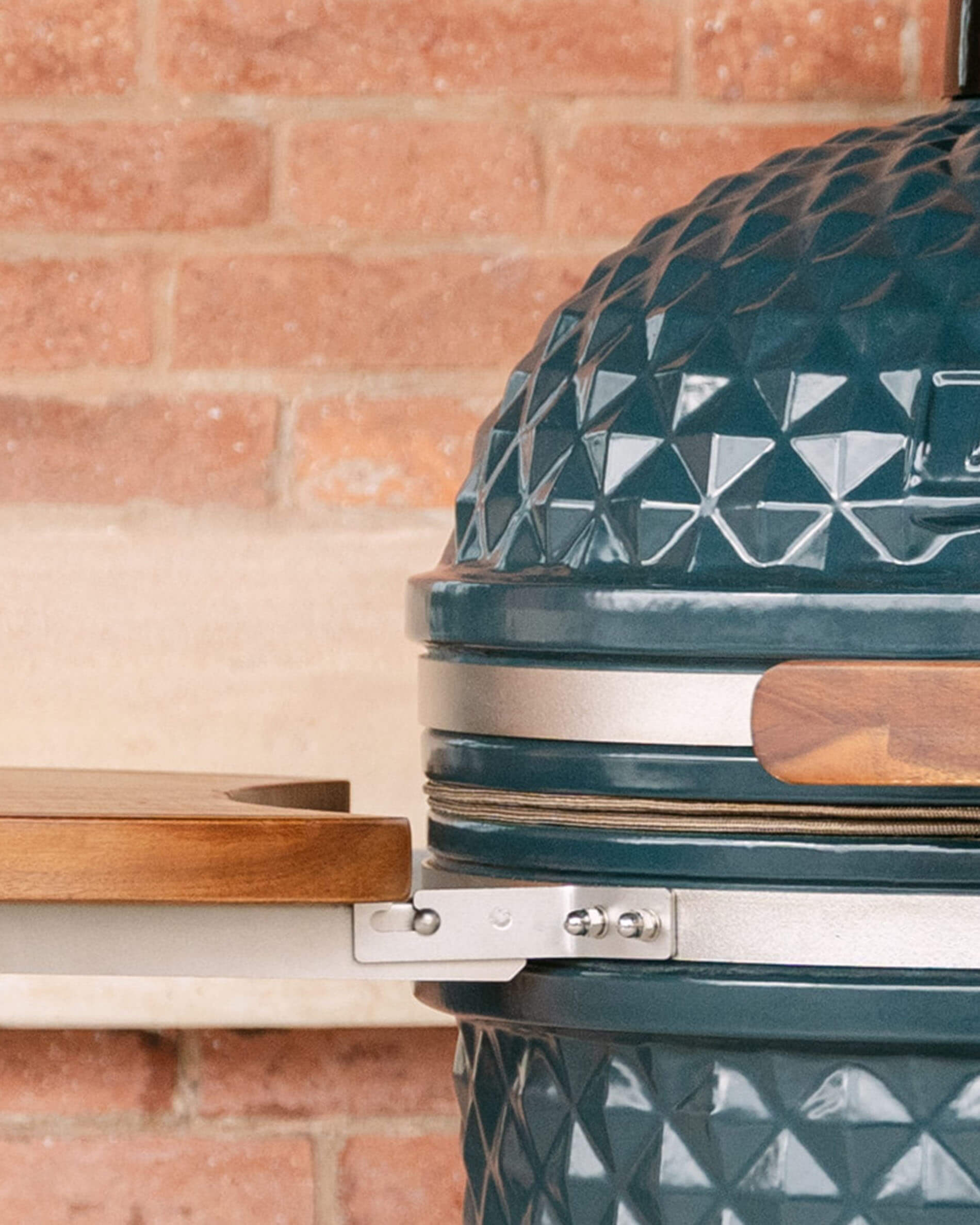 Dettaglio del fissaggio laterale di un ripiano in legno su kamado Kokko, che mostra il sistema di supporto metallico che collega il ripiano al corpo in ceramica.