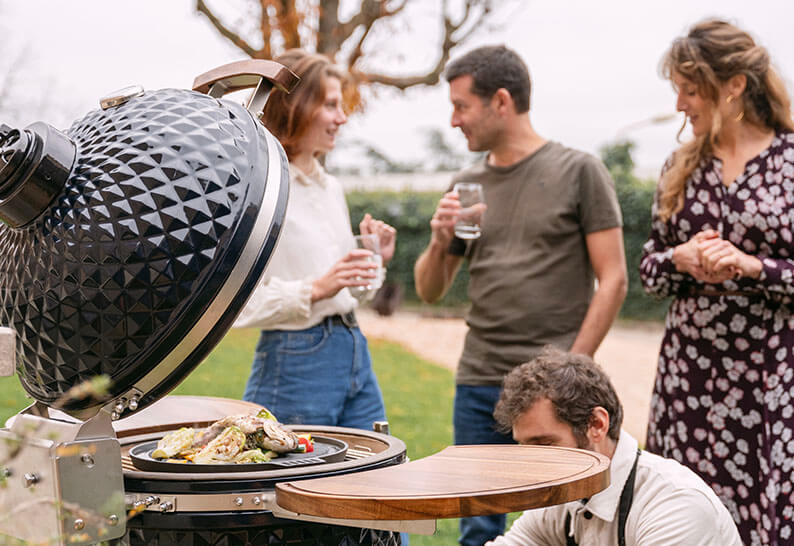 Groupe d’amis réunis autour d’un kamado Kokko lors d’un repas en extérieur, illustrant un moment de partage et de convivialité.