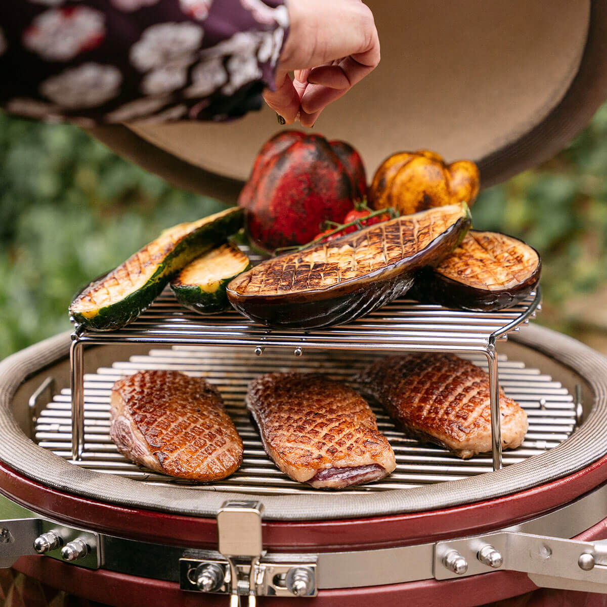 Cottura su due livelli in un kamado Kokko con petti d’anatra rosolati sulla griglia inferiore e verdure grigliate sulla griglia rialzata, a dimostrazione della versatilità di cottura.