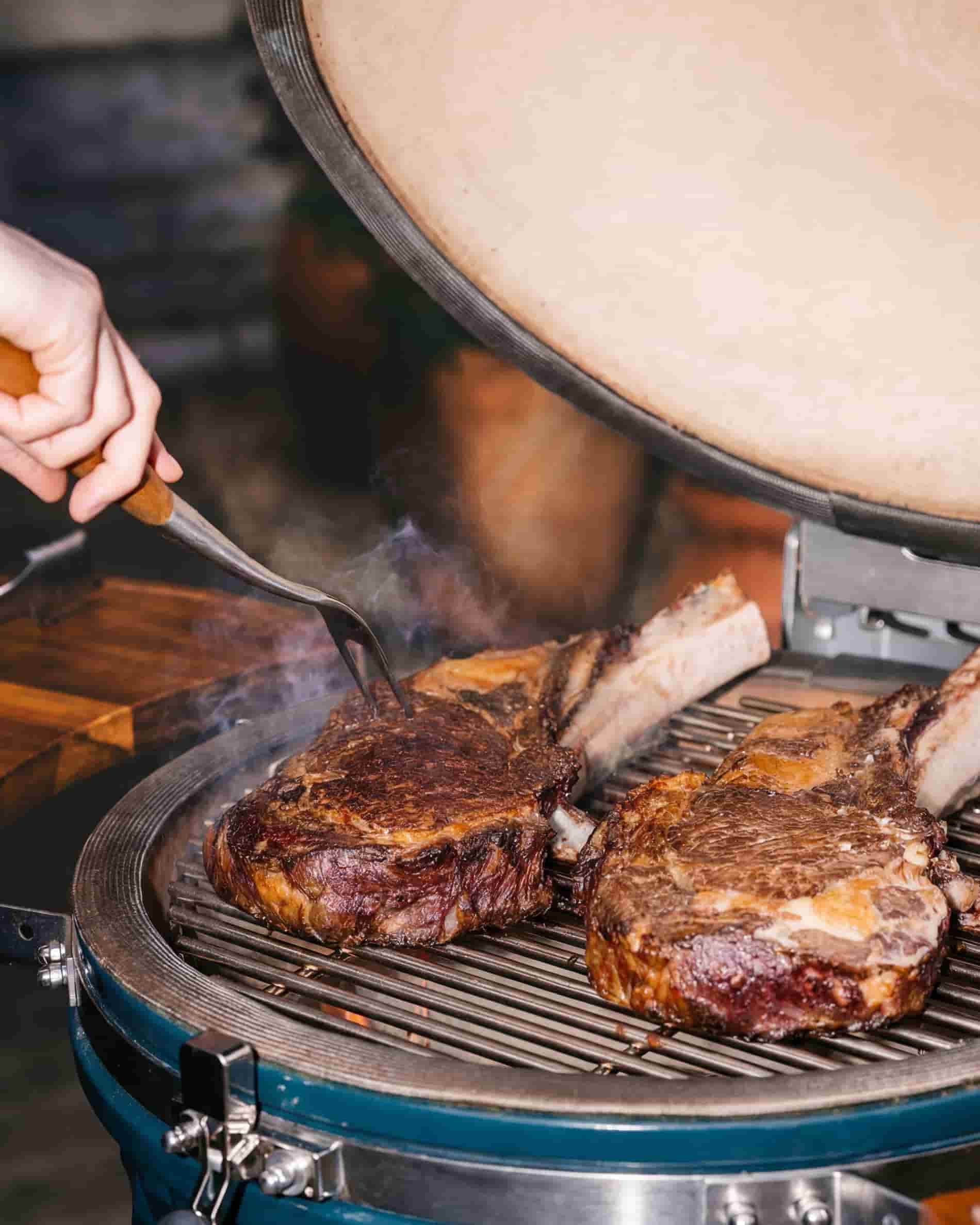 Cottura della carne sulla griglia di un kamado Kokko XL 22 pollici, coperchio aperto.
