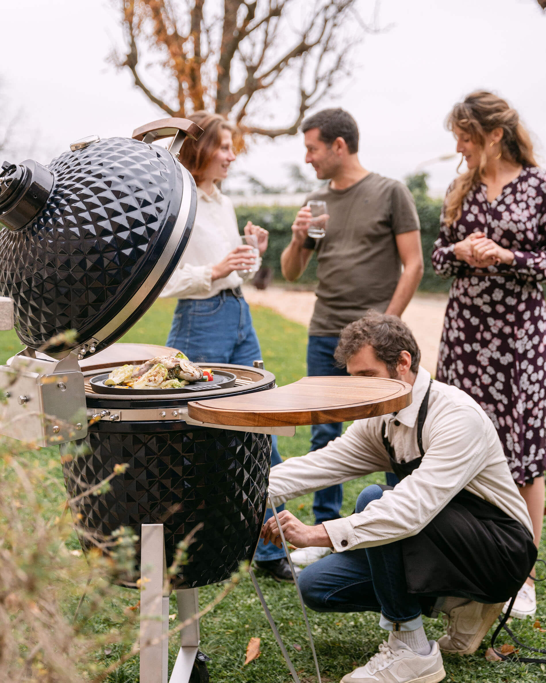 Kamado Kokko 22 pollici in ceramica blu navy utilizzato durante un momento conviviale all’aperto.