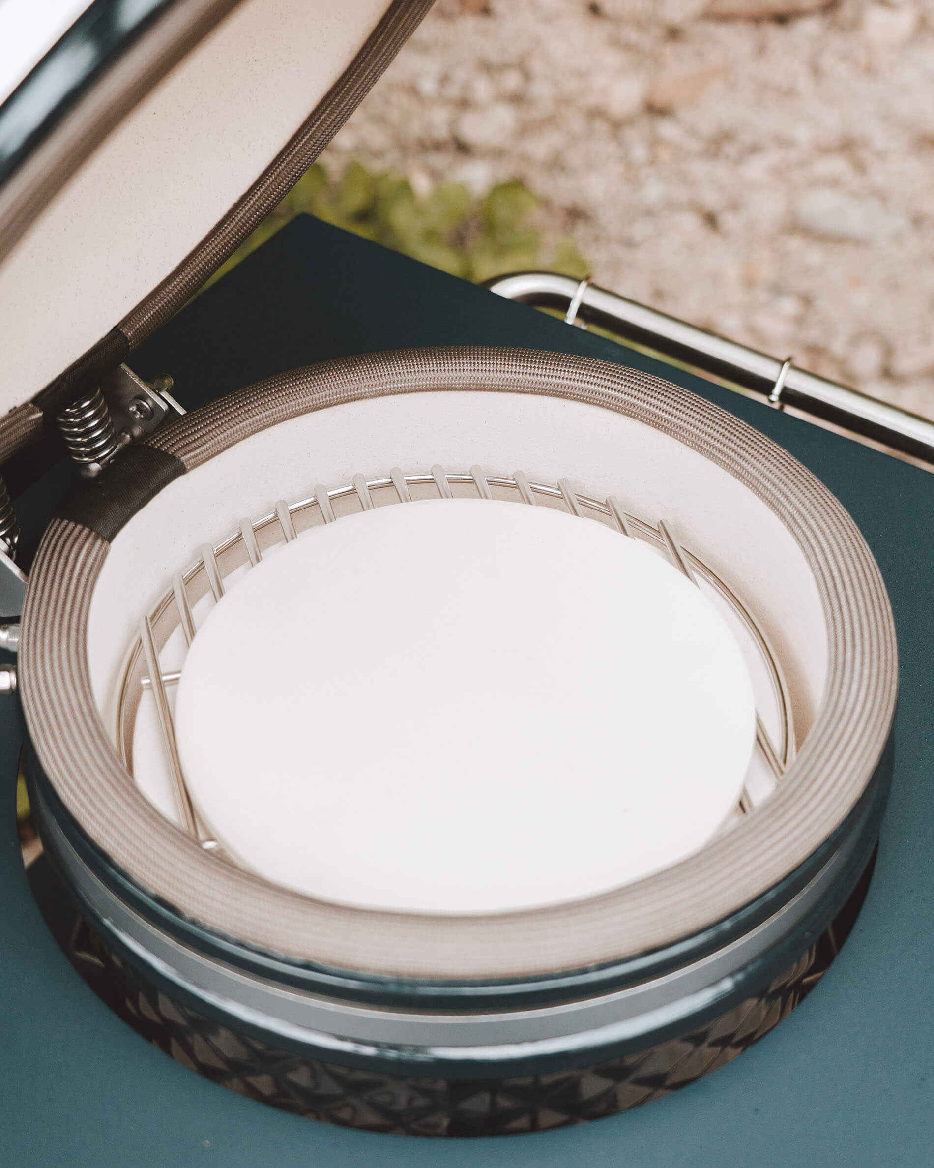 Interno del kamado Kokko con pietra refrattaria per pizza posizionata sul supporto di cottura, vista dettagliata della ceramica e della guarnizione di tenuta.