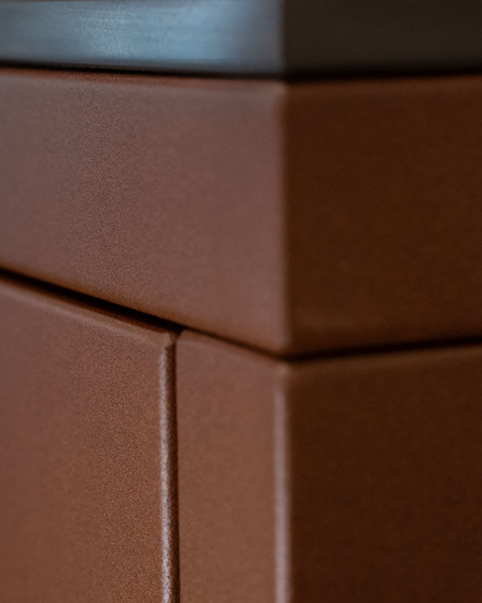 Dettaglio di finitura di una cucina su palafitte, con focus sull’angolo del mobile, l’assemblaggio dei pannelli e la texture opaca della facciata color ruggine.