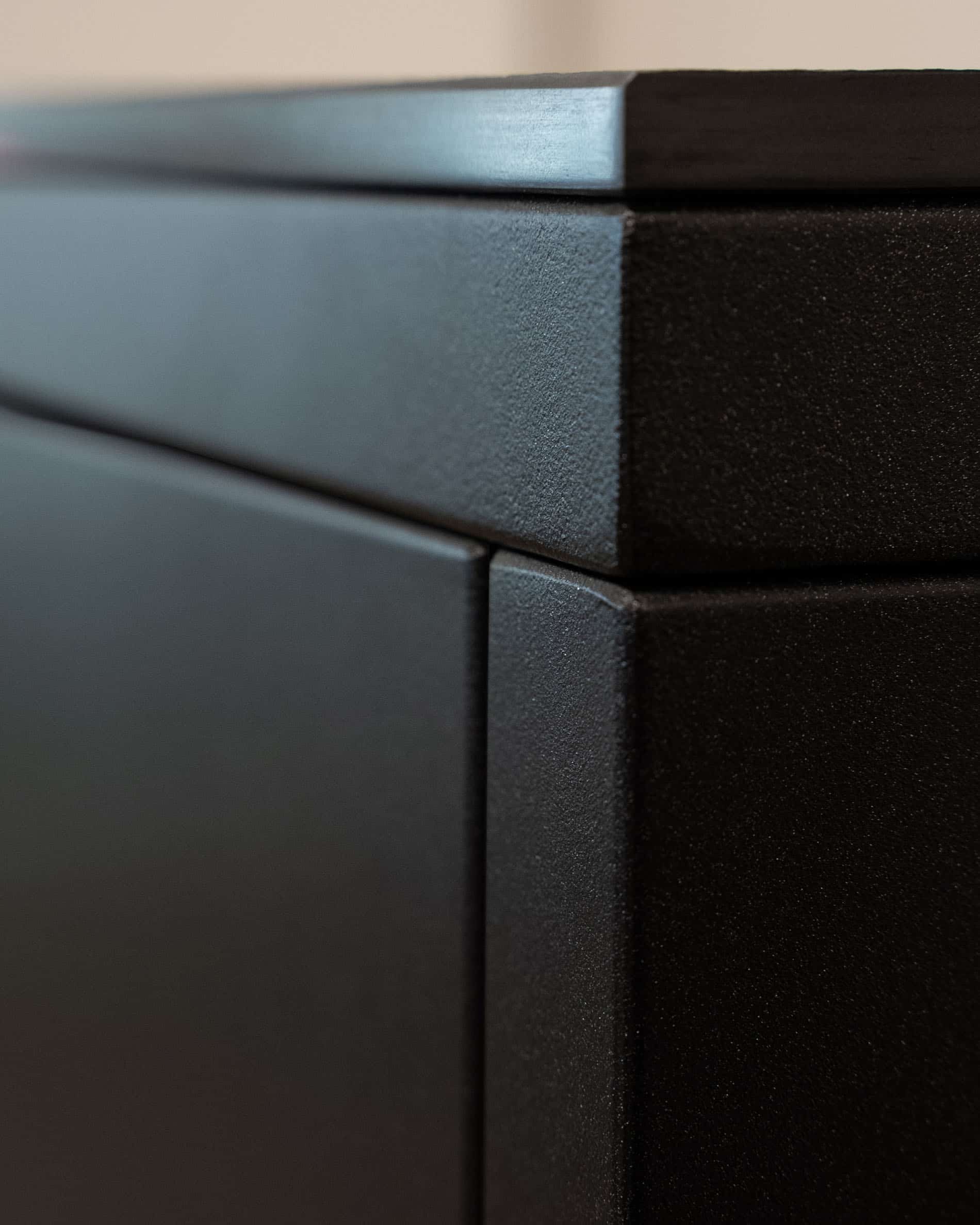 Dettaglio di finitura di una cucina su palafitte, con focus sull’angolo del mobile, l’assemblaggio dei pannelli e la texture opaca della facciata scura.