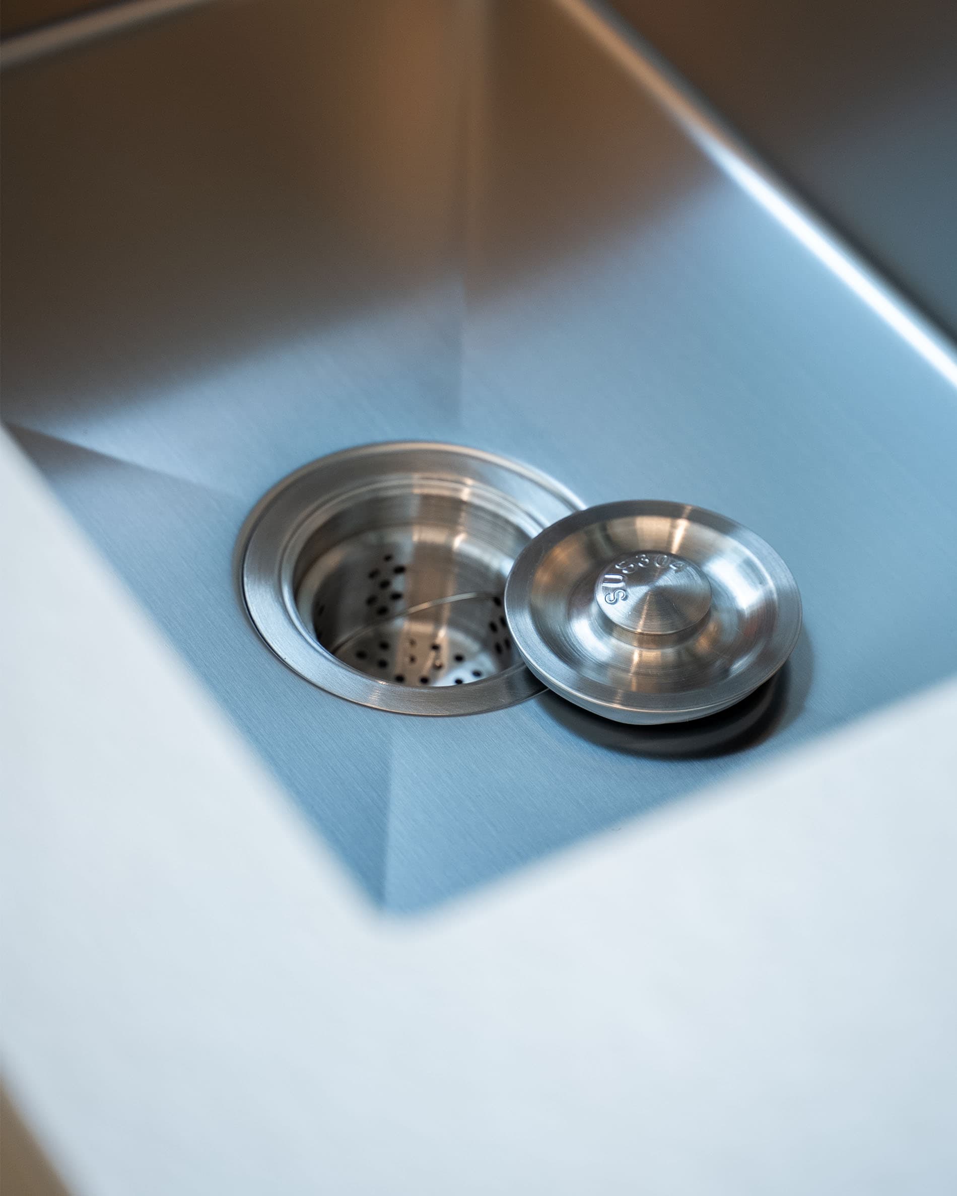 Dettaglio dello scarico del lavello di una cucina su palafitte, con vasca in acciaio inox e sistema di scarico integrato.