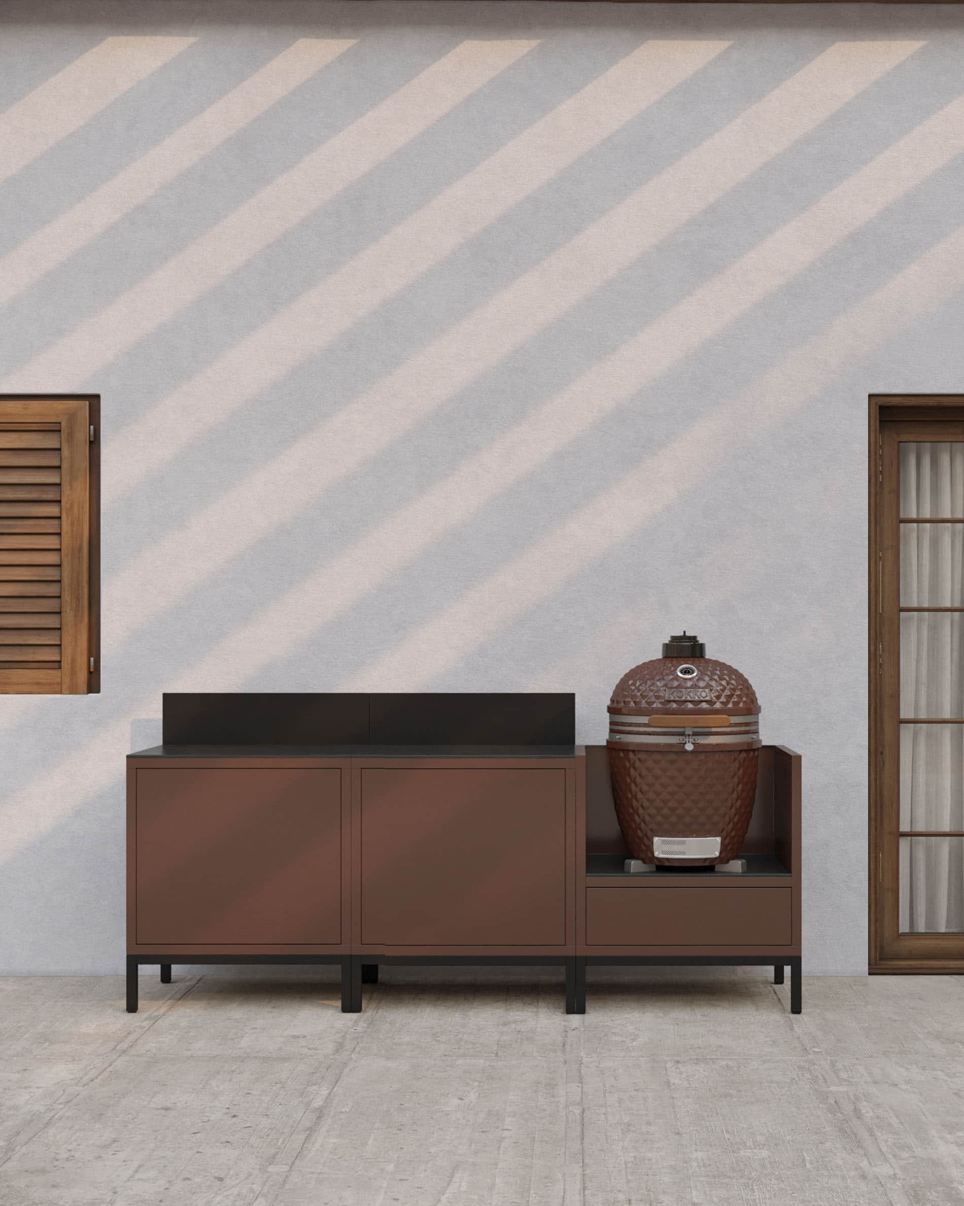Cucina su palafitte lineare color ruggine con piano di lavoro scuro, vani chiusi e modulo dedicato all’integrazione di un kamado per esterni.