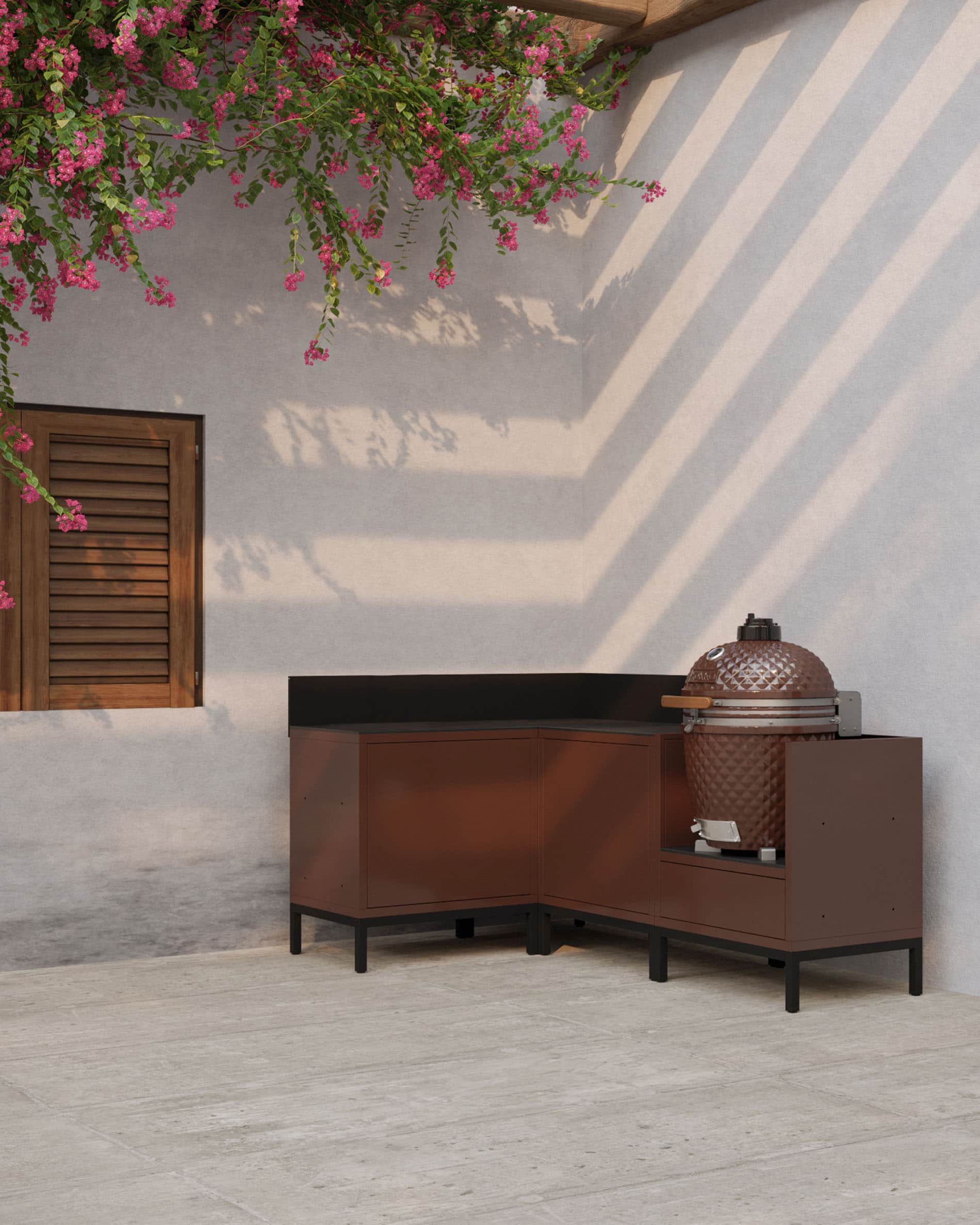 Cucina angolare su palafitte color ruggine con piano di lavoro scuro, vani chiusi e modulo dedicato all’integrazione di un kamado per esterni.