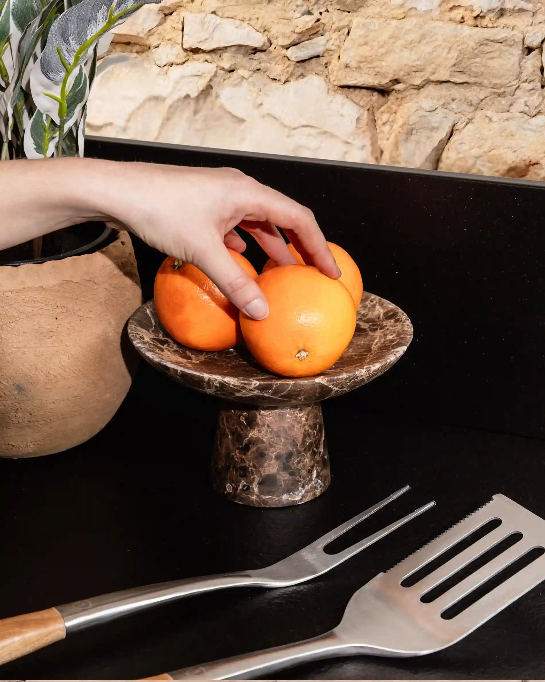 Mano che prende arance da un vassoio in pietra su cucina da esterno Kokko nera